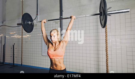 Muscular young woman doing weightlifting at crossfit gym. Fit female model lifting heavy weights at gym. Stock Photo