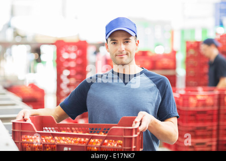 Portrait of confident worker holding crate of tomatoes in food processing plant Stock Photo