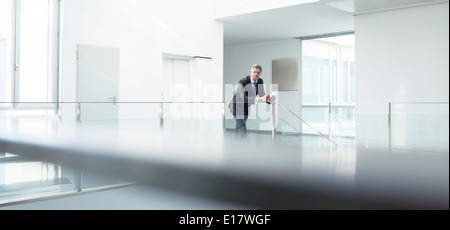 Businessman standing at railing in office Stock Photo