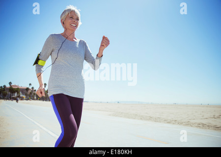 Senior woman jogging on beach boardwalk Stock Photo