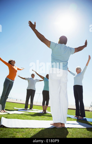 Seniors practicing yoga in sunny park Stock Photo