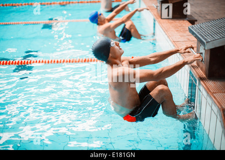 Swimmers poised at starting block in pool Stock Photo