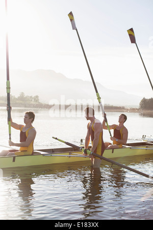 Rowing team lifting oars in lake Stock Photo