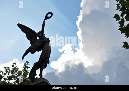 Shafts of light from the sun break through the clouds behind a statue of Victory on a war memorial near sunset Stock Photo