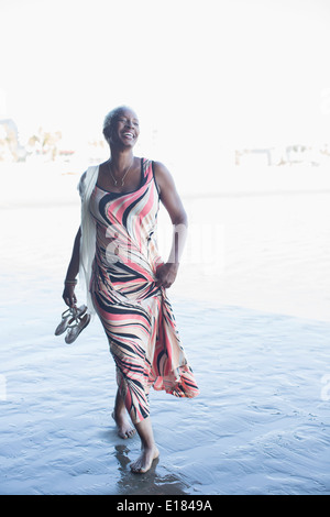 Happy woman in dress walking barefoot on beach Stock Photo