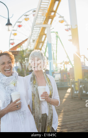 Senior women laughing and drinking coffee at amusement park Stock Photo