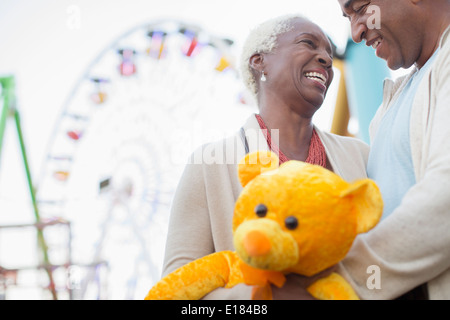 Senior couple with teddy bear hugging at amusement park Stock Photo