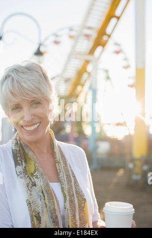 Portrait of smiling senior woman drinking coffee at amusement park Stock Photo