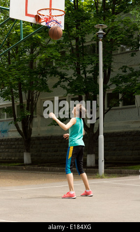 Young athletic teenage girl playing basketball practicing on her own as she scores a goal shooting the ball through the net Stock Photo