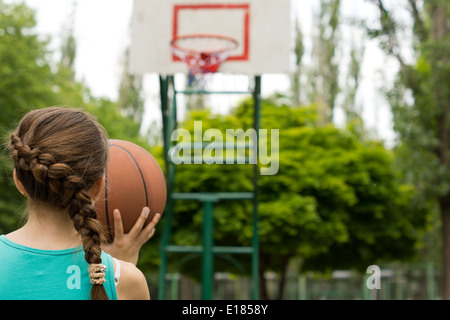 Young girl basketball player taking aim with the ball at the goal as she practices her game on an outdoor court Stock Photo