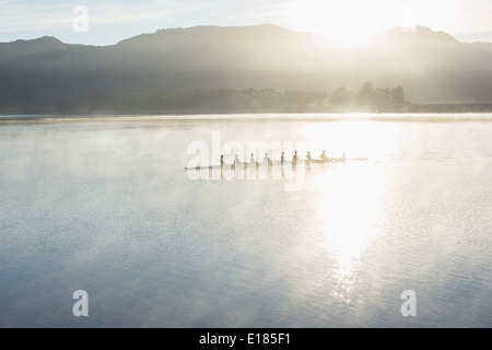 Rowing team rowing boat on still lake Stock Photo