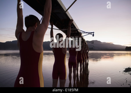 Rowing team carrying boat overhead into lake Stock Photo