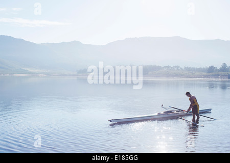 Man placing rowing scull in lake Stock Photo