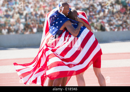 Track and field athletes wrapped in American flag on track Stock Photo