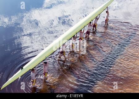 Rowing crew carrying scull overhead in lake Stock Photo