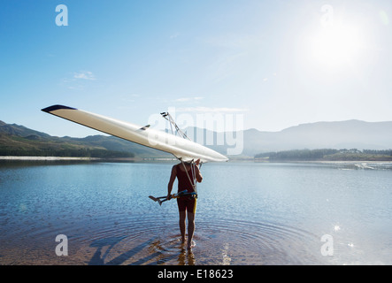 Man carrying rowing scull into lake Stock Photo