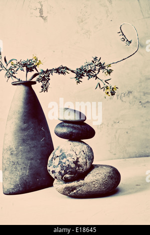 Zen Still life wabi sabi art photo. Balancing stacked stone next to a vase holding artful garden flowering branch. Stock Photo