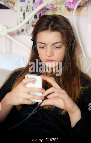 Teenage girl listening to music with headphones on her iphone on her bed in the bedroom. Stock Photo
