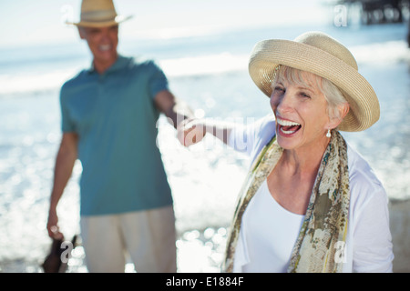 Enthusiastic senior couple holding hands on sunny beach Stock Photo
