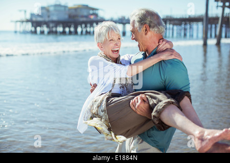Senior man carrying wife on sunny beach Stock Photo