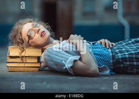 Funny crazy girl student with glasses lying on a pile of books outdoor Stock Photo