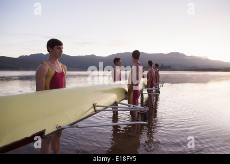 Rowing team holding scull in lake at dawn Stock Photo