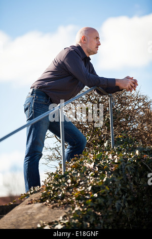 View from below of a thoughtful middle-aged man sitting on a flight of steps staring into the distance with a serious expression Stock Photo