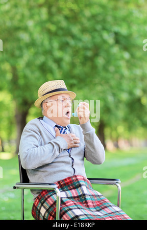 Senior man seated in wheelchair holding an inhaler and having an asthma attack Stock Photo