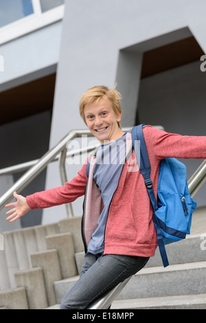 Excited teenage boy sliding down handrail on university stairway Stock Photo