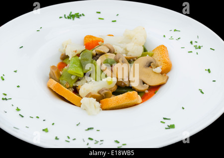 Spring vegetable stew in a white plate on black background. Stock Photo