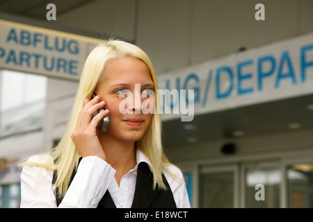Junge blonde Frau telefoniert mit dem Handy vor dem Abflug Stock Photo