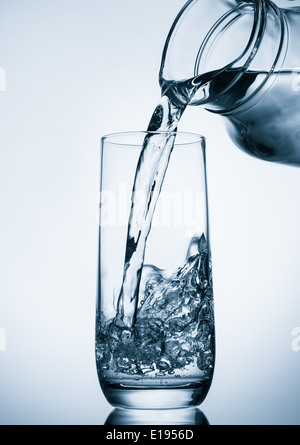 Pouring water from glass pitcher on blue background Stock Photo