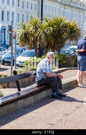 Elderly man, sitting on a wooden bench, with knotted handkerchief  on his head, Llandudno, North Wales Wales. Stock Photo