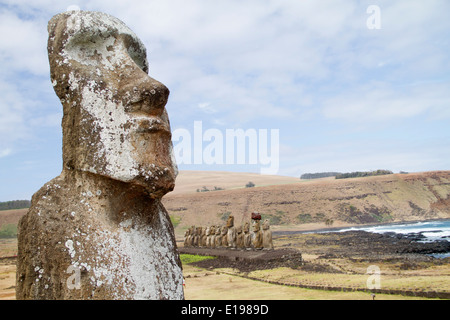 Closeup of face of giant carved stone statue and in the background fifteen statues called moai on a rock platform called abu Stock Photo