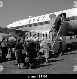 1950s Historical picture of a group of well dressed passengers boarding the steps onto a B.O.A.C airplane being supervised by an air stewardess Stock Photo