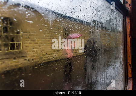 Looking out of a railway carriage wet window at a lady in pink coat and man in dark jacket Stock Photo