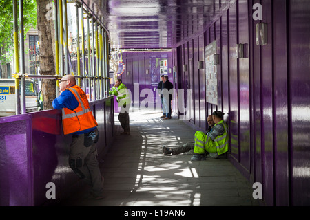 Builders taking a break in boarded safety path by construction site. Stock Photo