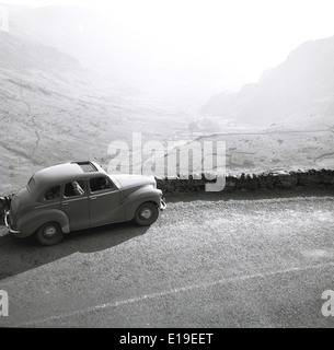 1950s historical picture showing a car parked on the side of a country road with a view down a misty valley, England. Stock Photo