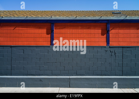Side of brightly colored building with orange insets and purple dividers between them, a gray concrete block wall. Stock Photo