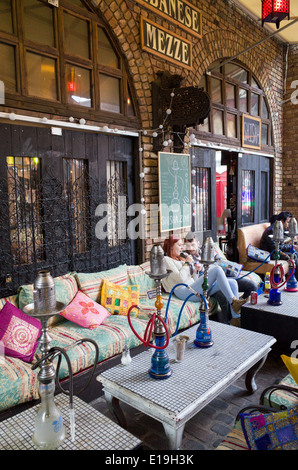 Young people smoking shisha pipes outside Lebanese restaurant in Camden Stables Market, London, England, UK Stock Photo