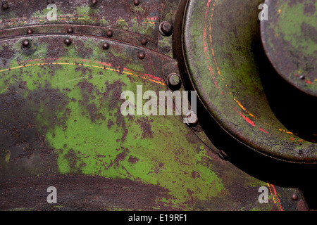 Riveted and bolted metal painted green lined in yellow and red colour, patches of rust showing through in places. Stock Photo