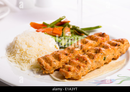 Chicken Adana kebap served with rice pilaf and green vegetables and some carrots Stock Photo