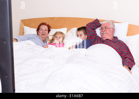 Grandparents watching TV in the bed with their grand kids, they look excited, perhaps its an adventure movie Stock Photo