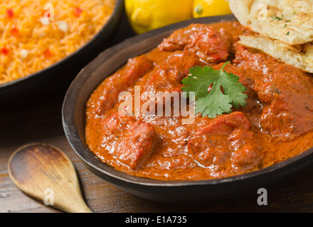 A delicious bowl of creamy chicken tikka masala with rice, lemons, and naan bread. Stock Photo