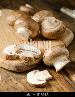 Delicious fresh mini bella crimini mushrooms on a rustic cutting board with knife. Stock Photo