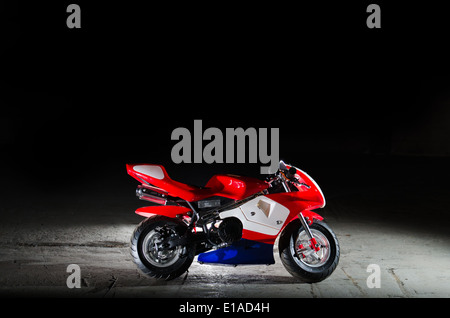 Photograph of a mini moto in a disused warehouse with a black background. Stock Photo