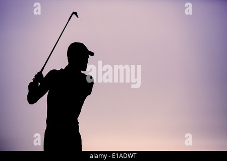 Golfer Swinging a Golf Club Silhouetted Against a clear Dusk Sky