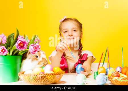 Girl colouring Eastern eggs and cute rabbit near Stock Photo