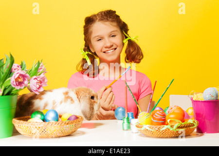 Girl paints Easter eggs with rabbit on the table Stock Photo