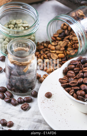 Green, brown unroasted decaf and black coffee beans in glass jars and cup. Stock Photo